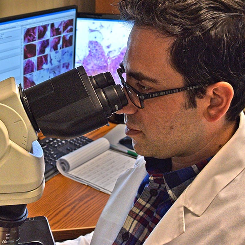 Male lab-tech looking at medical sample with microscope 